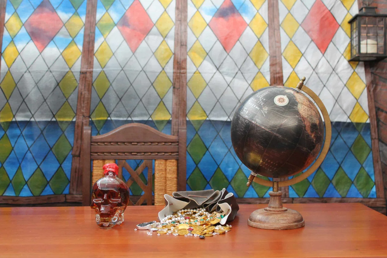 Décor de cabine de navire : vitrail en losanges colorés, globe terrestre, carafe en forme de crâne et pièces d'or sur une table