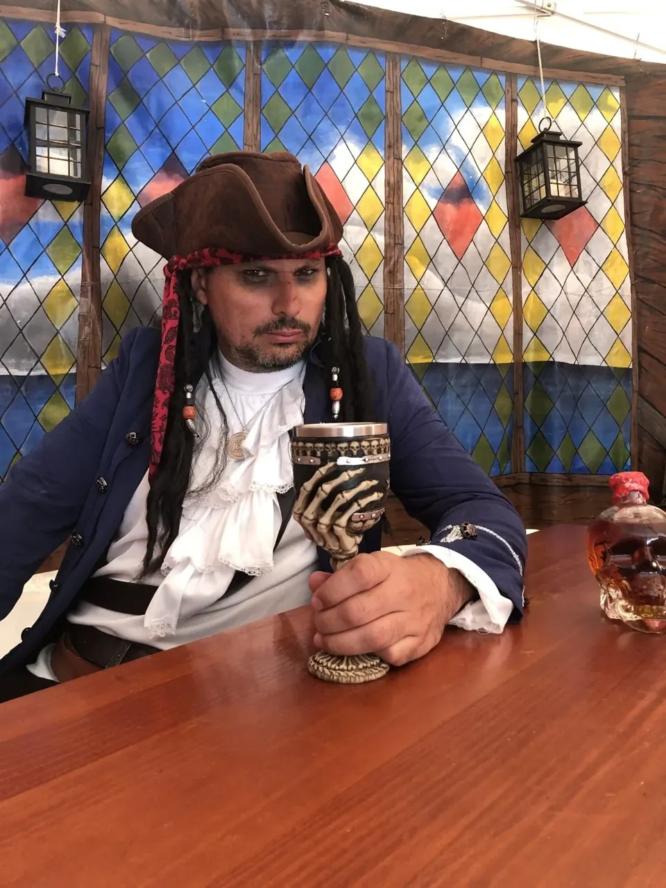 Pirate costumé tenant un calice en forme de crâne, assis à une table