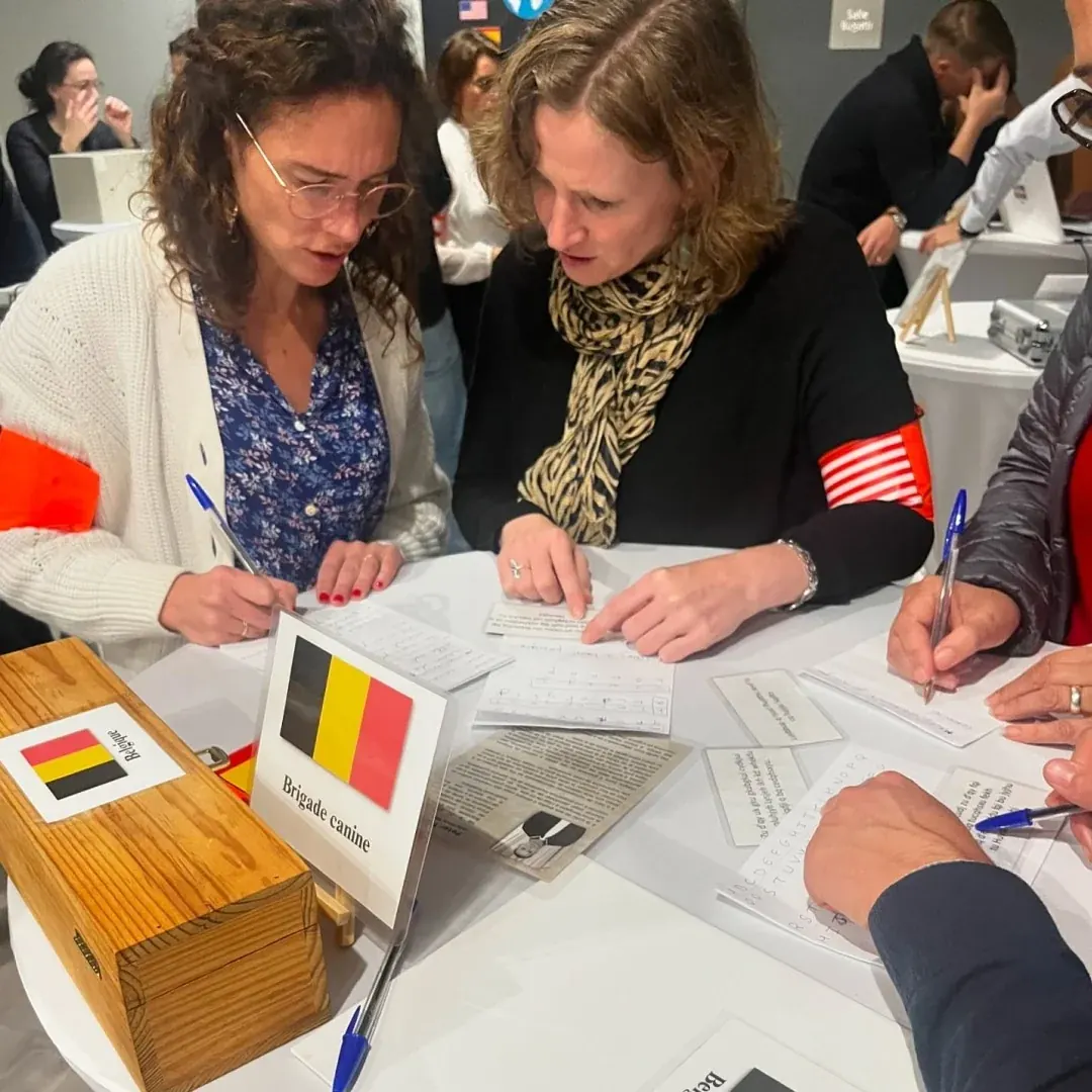 Deux joueuses remplissent un formulaire, devant un drapeau belge et un coffret en bois