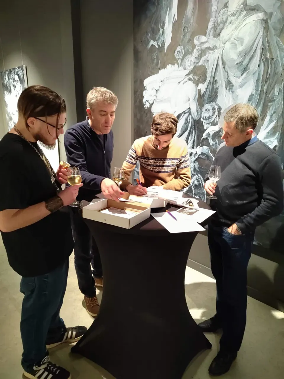 Quatre joueurs étudient des documents autour d'une table haute, dans une salle d'exposition